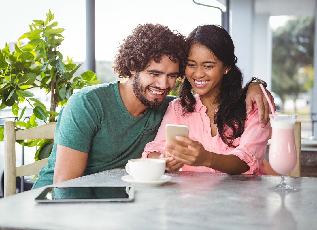 About Our Agency - Couple Looking at Mobile Phone Whiling Smiling and Drinking Smoothies